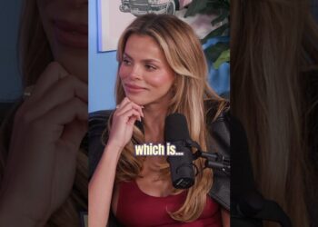 Mujer rubia sentada frente a un micrófono en un estudio, mirada pensativa y gesto elegante