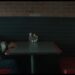 Hombre calvo sentado solo en un puesto de restaurante tipo diner frente a una mesa con condimentos.