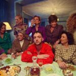 Dónde vive C. Tangana: descubre su hogar y estilo de vida en una escena de cena íntima con un hombre de camisa roja rodeado de varias mujeres en un comedor clásico