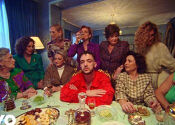 Dónde vive C. Tangana: descubre su hogar y estilo de vida en una escena de cena íntima con un hombre de camisa roja rodeado de varias mujeres en un comedor clásico