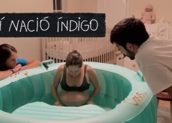 Mujer en trabajo de parto dentro de una piscina inflable en una habitación con cuna, acompañada por dos personas