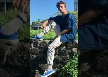Descubre por qué Amanda Seyfried no se separó de estas zapatillas blancas en el Festival de Venecia; joven sentado sobre un muro de piedra con zapatillas azules, calcetines blancos y ropa informal.
