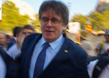 Hombre con traje y corbata entre una multitud en un acto urbano al aire libre, con movimiento desenfocado