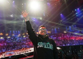 DJ sonriente en tarima frente a una multitud iluminada por focos y pantallas, ¿Cuánto cobra Carlos Herrera? Descubre su salario millonario en radio.