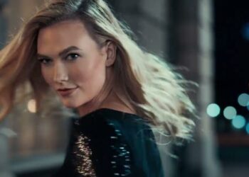 Mujer rubia girando la cabeza hacia la cámara en un ambiente urbano nocturno con luces desenfocadas