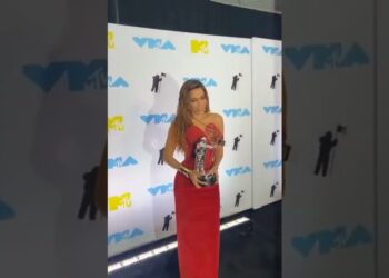 Mujer en un elegante vestido rojo sostiene un trofeo frente a un photocall con logotipos VMA/MTV en una alfombra; Las nominaciones a los Emmy 2025 ya están aquí y te sorprenderán: descubre qué series han arrasado con las nominaciones en tiempo real