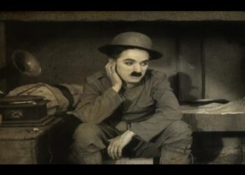 Actor cómico en blanco y negro sentado con sombrero y bigote distintivo, expresión pensativa