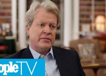 Hombre rubio de mediana edad en una entrevista en interiores con estanterías y el logo de PeopleTV visible
