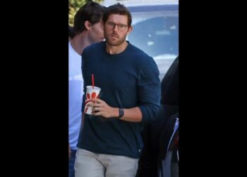 Hombre joven con gafas y camiseta azul sosteniendo un vaso con popote, mostrando una notable apariencia delgada y cambio físico visible