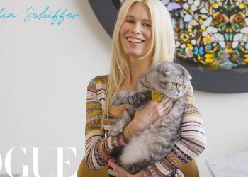 Modelo rubia de 21 años deslumbrante con un corset que deja sin aliento, sonriente y sosteniendo un gato gris