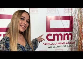 Mujer sonriente señalando el logotipo de Castilla-La Mancha Media en un photocall