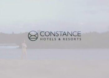 Descubre por qué Constance Prince Maurice es el hotel más deseado de la deliciosa Mauricio: logotipo de Constance Hotels & Resorts sobre una playa tranquila con una persona caminando junto al agua.