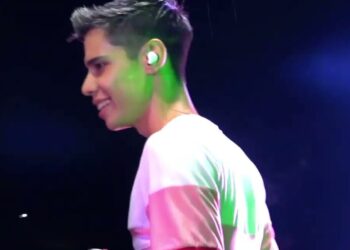 Joven cantante en perfil sonriendo con monitor intraauricular y luces verdes y moradas sobre un escenario oscuro; El inesperado viaje de la princesa Diana que transformó un pueblo francés en el nuevo destino de las estrellas