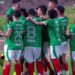 Jugadores de fútbol con uniformes verdes y medias rojas celebran en el campo tras un gol, aficionados graban con el móvil; ¿Cuánto dinero tiene TheGrefg? Descubre su fortuna y secretos
