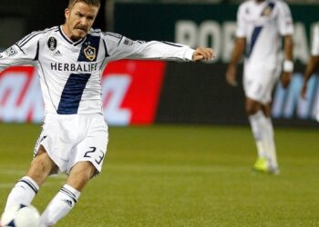 Jugador de fútbol del LA Galaxy con uniforme blanco y balón en movimiento ejecutando un disparo