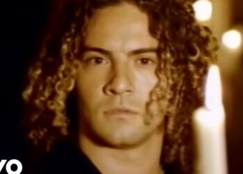 Primer plano de un cantante de rizos junto a una vela en ambiente íntimo; ¿Cuánto cobra este artista por concierto? Descubre su caché real