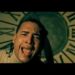 Cantante masculino en primer plano frente a un gran reloj, expresión intensa y estética de videoclip