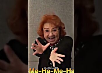 Mujer mayor con cabello naranja y gafas haciendo un gesto dramático con las manos extendidas; ¿Dónde vive Goku? Descubre su hogar y secretos en Dragon Ball