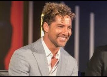 Retrato de un hombre sonriente con traje claro en un escenario iluminado, expresión cálida y actitud profesional