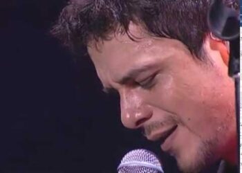 Primer plano de un cantante masculino interpretando una canción frente a un micrófono en un escenario.