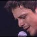Primer plano de un cantante masculino interpretando una canción frente a un micrófono en un escenario.