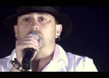 Cantante con sombrero y micrófono en primer plano, Caché de El Barrio: Descubre cuánto cuesta contratarlo hoy