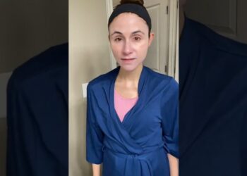 Mujer de pie frente al espejo con bata azul y diadema negra; Descubre por qué el protector solar que adora Kyle Richards se ha convertido en mi nueva obsesión.
