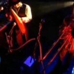Concierto íntimo en escenario con músicos, luces rojas y azules y micrófonos: ¿De dónde es Bunbury? Descubre sus raíces y su historia musical