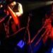 Músicos en escena con iluminación roja y azul, micrófonos, cables y una trompeta; Dónde vive Enrique Bunbury: descubre su hogar y estilo de vida