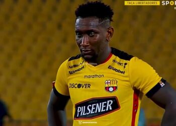 Jugador de fútbol con camiseta amarilla y expresión seria frente a tribunas desenfocadas, La familia de Eric del Castillo: amor, legado y sorpresas emocionantes