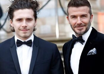 Hombre joven con esmoquin junto a un hombre mayor en traje de gala, rinde emotivo homenaje a la abuela de su esposa mientras surgen rumores de tensión familiar.