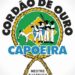 Logo de Cordão de Ouro con siluetas de capoeira sobre un mapa de Brasil enmarcado por una cuerda; Descubre la fascinante historia de la familia Ouro y su legado.