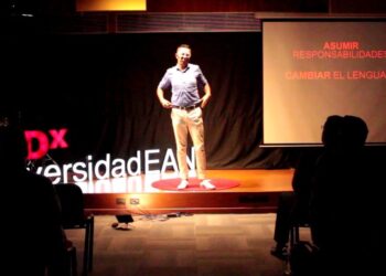 Conferencista de pie en el escenario TEDx de la Universidad EAN junto a una pantalla que muestra 'ASUMIR RESPONSABILIDADES' y 'CAMBIAR EL LENGUAJE'.