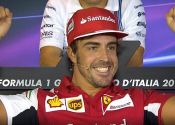 Piloto de automovilismo sonriente con gorra y camiseta roja celebrando con los brazos en alto, ¿Cuánto cobra este piloto? Descubre su sorprendente salario