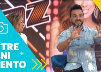 Presentador en un set de televisión sonriendo y gesticulando junto a una gráfica azul de entretenimiento.