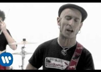 Vocalista rockero en primer plano con gorra, pendientes y correa de guitarra, estética asociada a fito fitipaldis