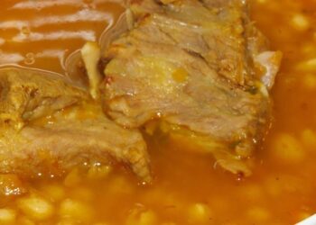 Descubre los 8 alimentos ricos en potasio que los nutricionistas recomiendan para aliviar cólicos y hinchazón menstrual en un plato de guiso de alubias blancas con trozos de carne en caldo anaranjado.