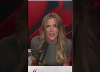 Mujer rubia hablando frente a un micrófono en un set de grabación con fondo rojo y negro, mostrando una expresión de sorpresa.