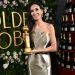 Mujer elegante sostiene un trofeo dorado frente al logo de los Golden Globes y una torre de botellas de champán, Descubre cómo conseguir boletos de los Golden Globes por $70,000 y lo que realmente hay detrás de este extravagante regalo de Penske Media