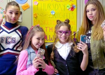 Cuatro chicas en un pasillo escolar sosteniendo móviles con fundas brillantes, evocando el estilo gossip girl.