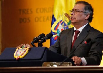 Hombre con traje dando un discurso en un atril con el escudo y la bandera de Colombia