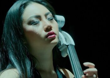 Mujer concentrada tocando un violonchelo eléctrico en primer plano, ¿Cuánto cobra Hans Zimmer? Descubre su impresionante fortuna