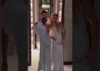 Dos personas posando frente a un espejo con vestidos largos blancos y elegantes, transmitiendo un estilo de gala y un aire de ensueño.