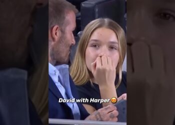 Padre y hija en un evento deportivo, ella con la mano en la boca en gesto pensativo y él con tatuajes junto a ella.