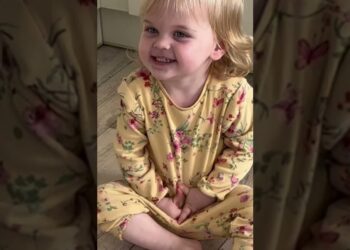 Niña pequeña sonriente sentada en el suelo con pijama amarilla de estampado floral