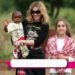 Los sorprendentes caminos de los hijos de Madonna hoy en día: mujer rubia con gafas sostiene a un niño pequeño mientras una niña sonríe a su lado en un entorno al aire libre