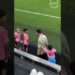 Niños con camisetas rosas y números en la grada de un estadio observando el campo