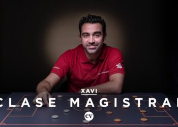 Entrenador no identificado sentado frente a un tablero táctico iluminado, en pose explicativa.