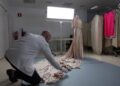 Conservador con guantes arregla el largo vestido sobre el suelo junto a un maniquí; ¿De dónde es Balenciaga? Descubre sus raíces vascas y legado