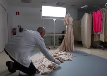Conservador con guantes arregla el largo vestido sobre el suelo junto a un maniquí; ¿De dónde es Balenciaga? Descubre sus raíces vascas y legado